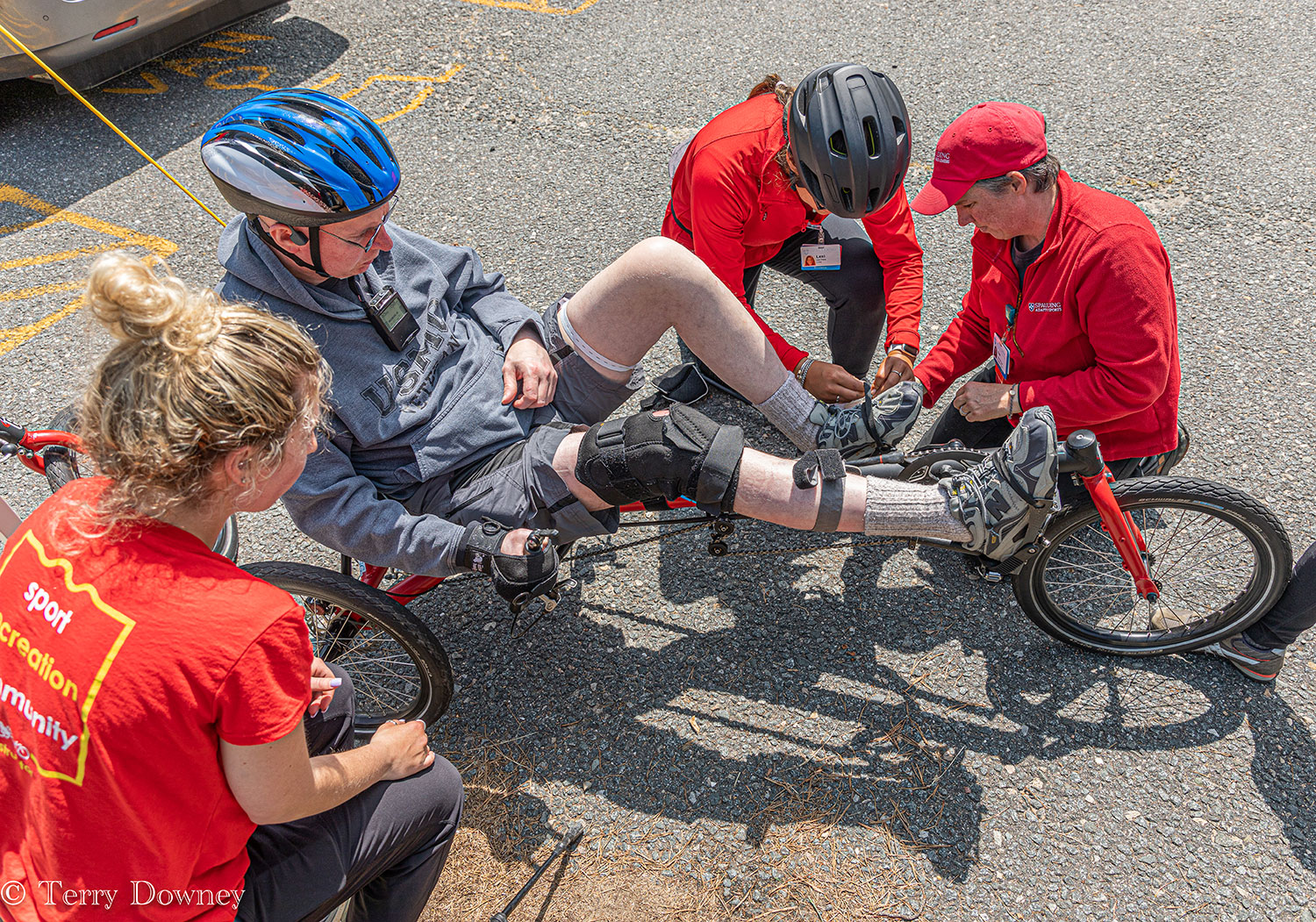 Three therapists help an older man strap into an adaptive bicycle.
