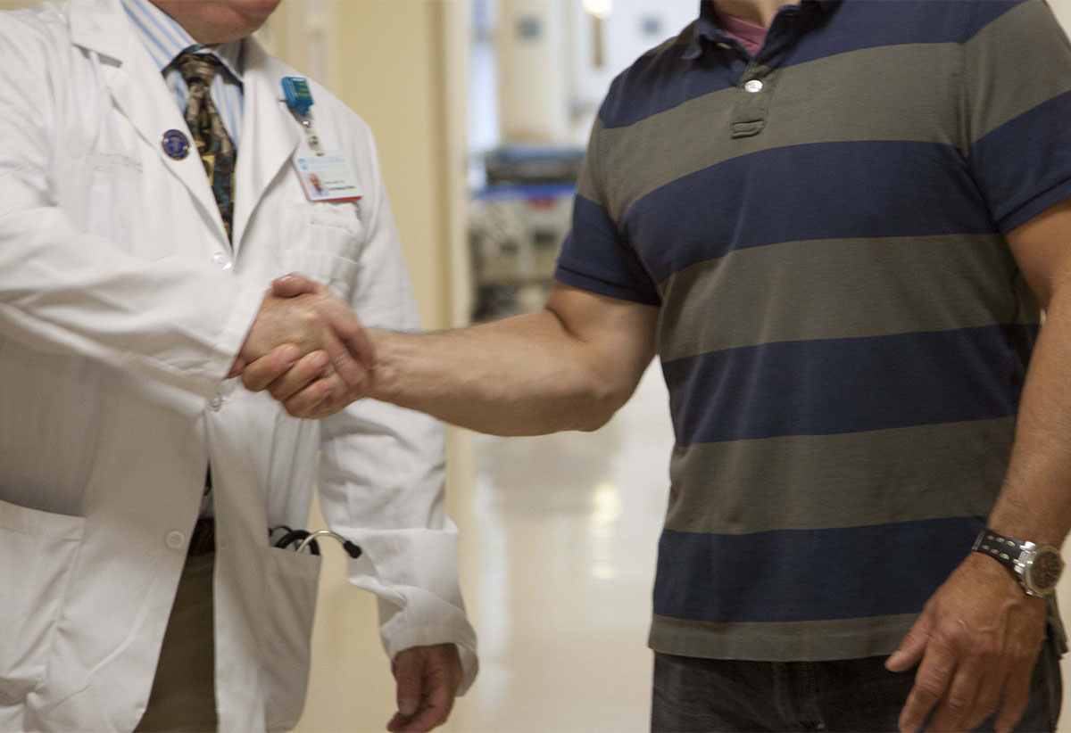 A doctor and a strongly built man shake hands.