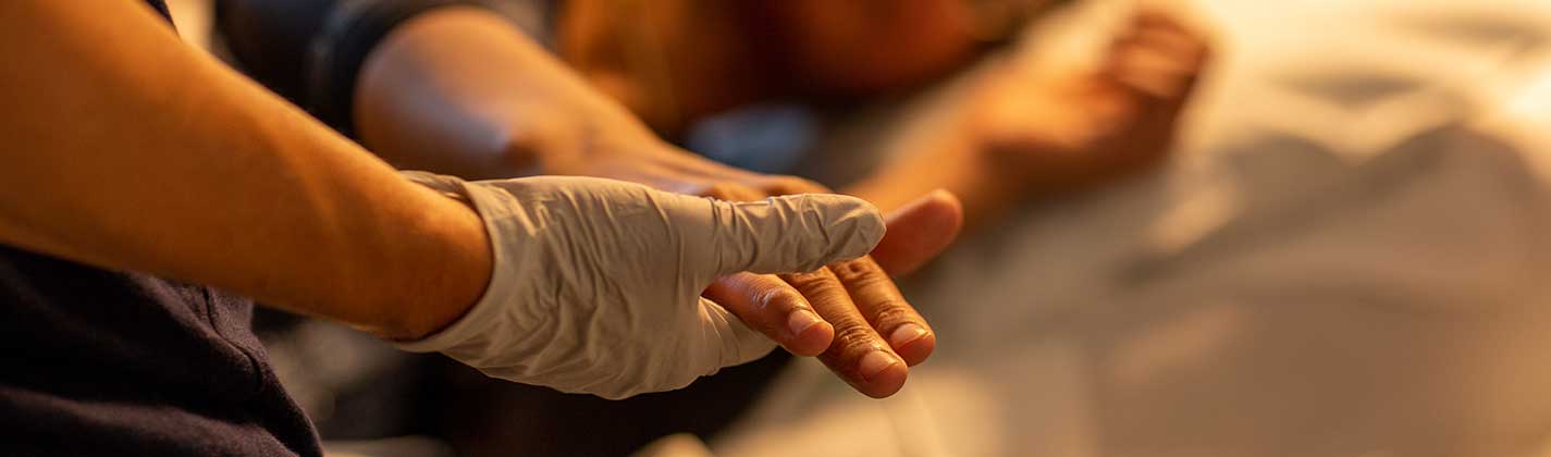 Closeup on a nurse's gloved hand holding a patient's hand.