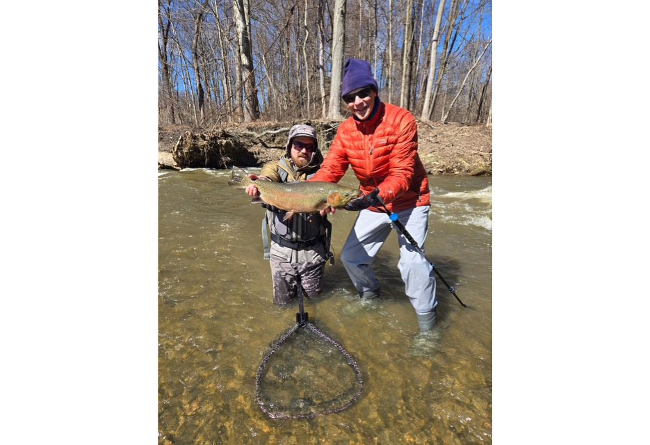 John and a friend stand in a wintry stream, holding up a freshly caught fish.