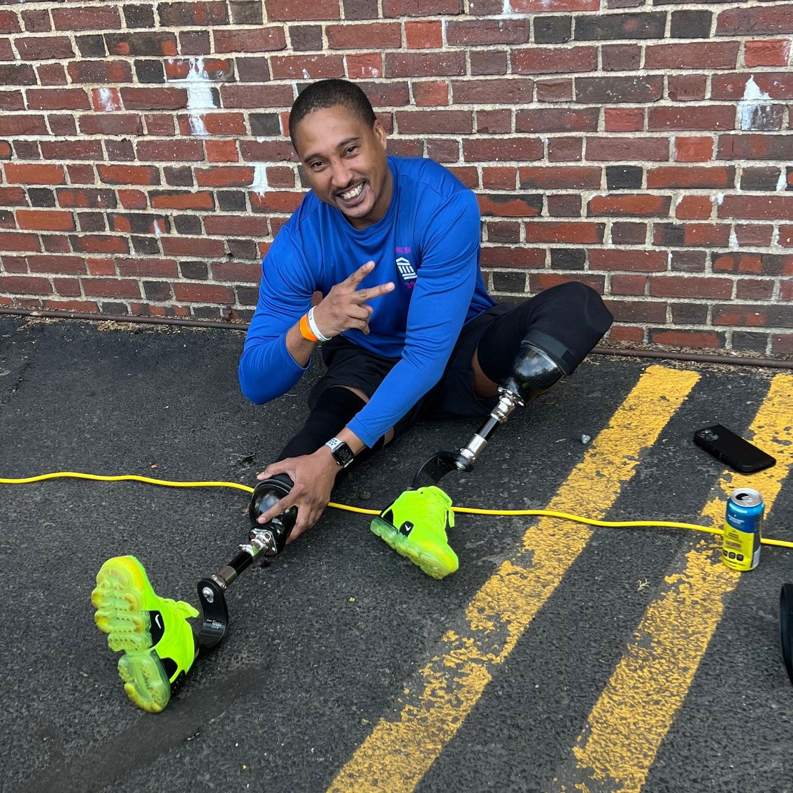 A smiling man stretching while wearing two lower-leg prostheses with neon yellow sneakers.