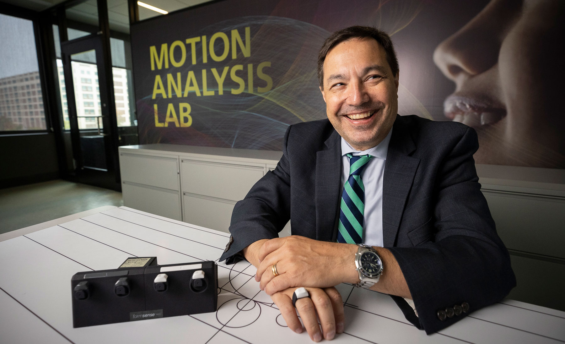 Paolo Bonato displaying a piece of equipment in front of a banner that says Motion Analysis Lab.